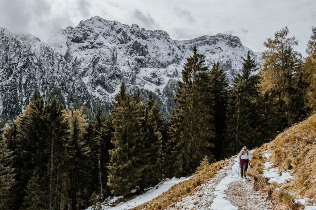 A person hikes on a snowy trail with snowy mountains in the background